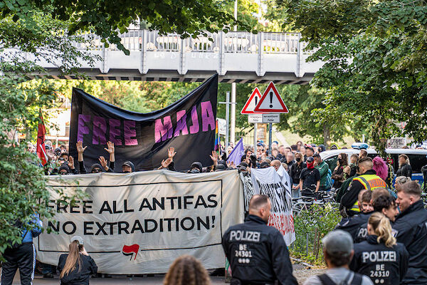 Das Foto von © Björn Obmann zeigt die Demonstration mit dem Frottransparent "Free all Antifas from Extradition!" dahinter das Transparent "Free Maja!" rechts im Bild einige Bullen mitsamt ihrer Wanne