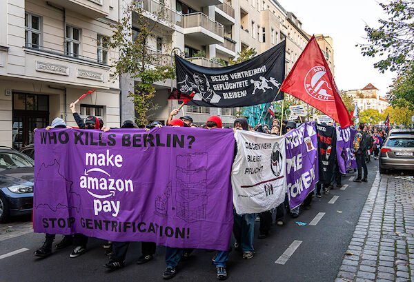 Die Demo mit dem Fronttransparent "Who kills Berlin? Make Amazon pay - Stop Gentrification!" einem Hochtransparent mit dem Text "Bezos vertreiben - Geflüchtete bleiben!" und mehreren Seitentransparenten.