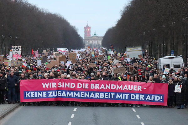 Das Foto von © Kinkalitzken zeigt das Fronttransparent der Demo mit dem Text "Wir sind die Brandmauer - Keine Zusammenarbeit mit der AfD!" auf der Straße des 17. Juni, hinter dem sich Massen von Menschen bis hin zumBrandenbruger Tor versammelt haben