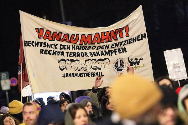 Das Foto zeigt ein Transparent mit dem Text: "Hanau mahnt! Rechtsruck den Boden entziehen - rechten Terror bekämpfen" sowie Portraits von Gökhan Gültekin, Sedat Gürbüz, Said Nesar Hashemi, Mercedes Kierpacz, Hamza Kurtović, Vili Viorel Păun, Fatih Saraçoğlu, Kaloyan Velkov und Ferhat Unvar und dem Hashtag #HanauIstÜberall