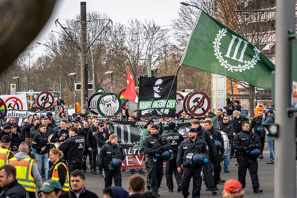 Das Foto von © Björn Obmann zeigt die Demo des III. Wegs in Hellersdorf, der von ein paar Polizist:*Innen angeführt wird.Die Faschisten tragen Tafeln mit durchgestrichenem Hammer und Sichel ete. etc. etc.