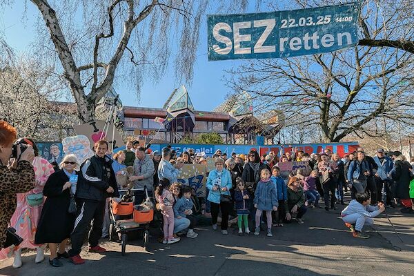 Das Foto zeigt einen Teil der Protestierenden vor dem SEZ mit darüber hängendem Transparent mit dem Text "SEZ 22.03.25 retten"