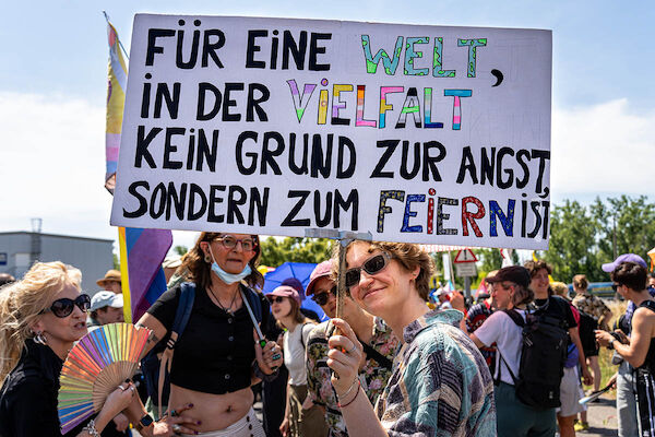 Das Foto zeigt Teilnehmer der Pride, eine Person hält eine Texttafel hoch: "Für eine Welt, in der Vielfalt kein Grund zur Angst sondern zum Feiern ist"