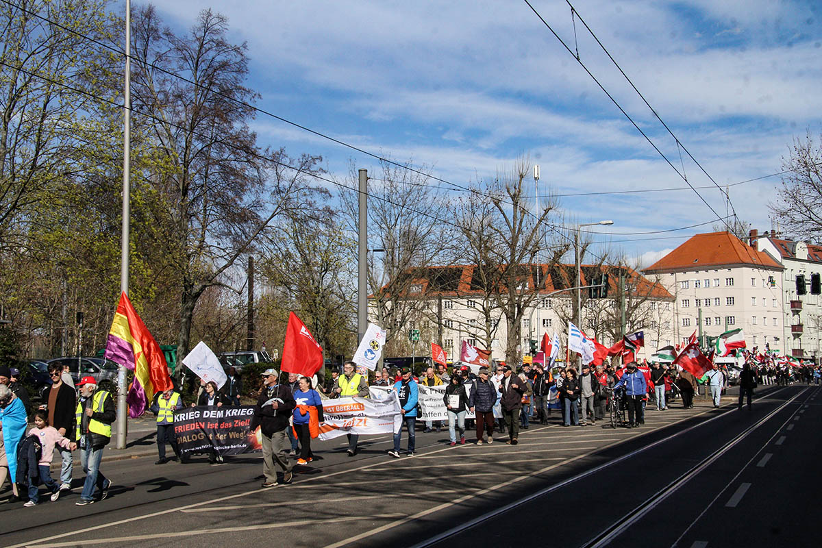 Das Foto zeigt eine Weitwinkelaufnahme eines Teils des Ostermarsches mit verschiedenen Transparenten, unter anderem Freiedensglocke, DKP, IG MEtall, BSW,
