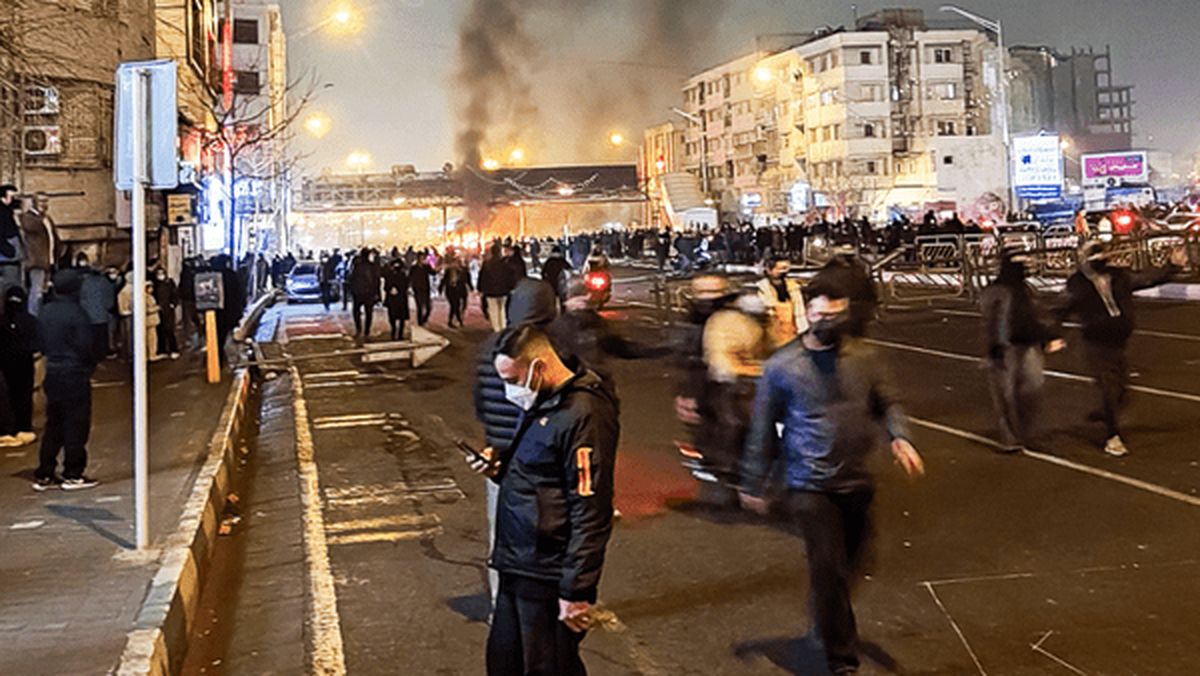 Das Foto zeigt Menschenmassen auf einer Straße, im mittleren Hintergrund eine brennende Barrikade