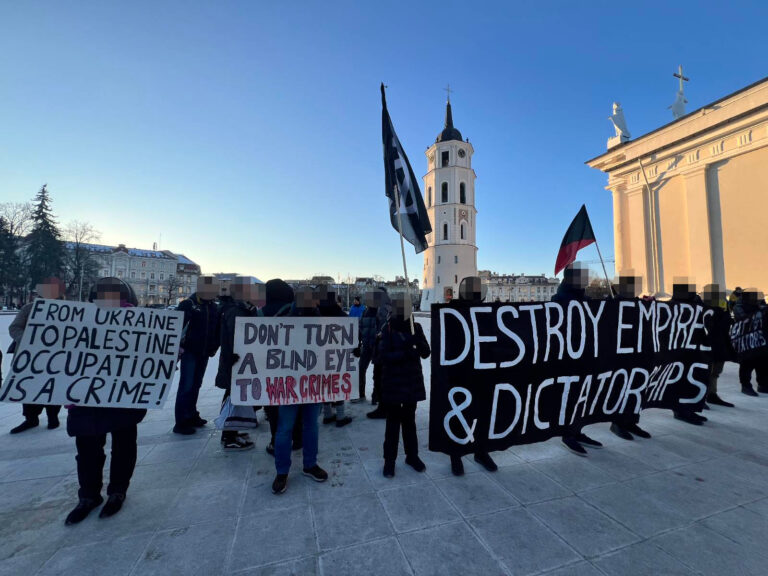 Das Foto zeigt verschiedene Personen mit Transparenten und Texttafeln. Auf einem schwarzen Transparent steht: "Destroy Empires & Dictatorships" links davon auf einer Texttafel: "Don't turn a blind Eye to War Crimes" sowie "From Ukraine to Palestine - Occupation is a Crime!"